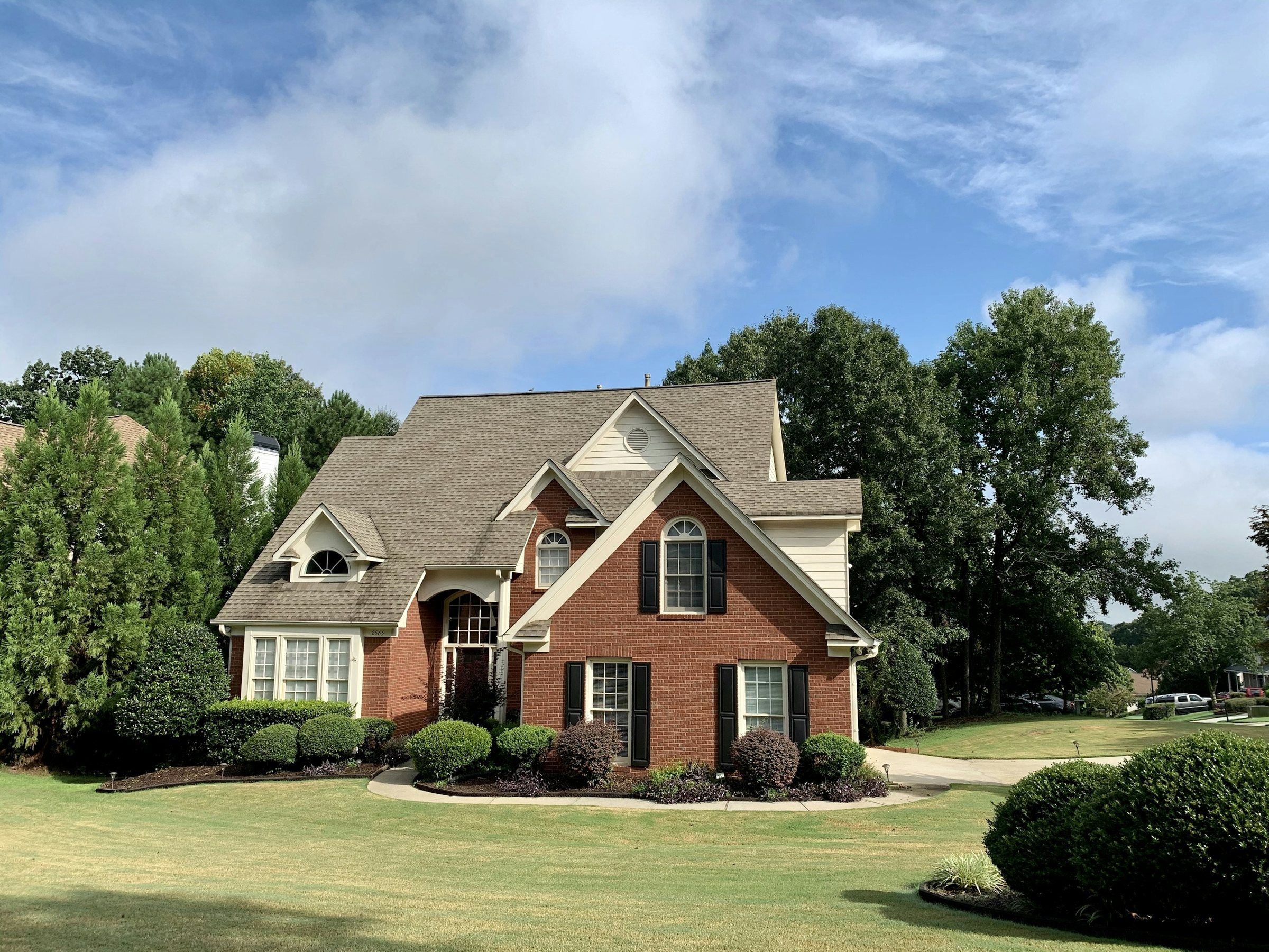 Brick two-story home with a brown architectural shingle roof under a blue sky