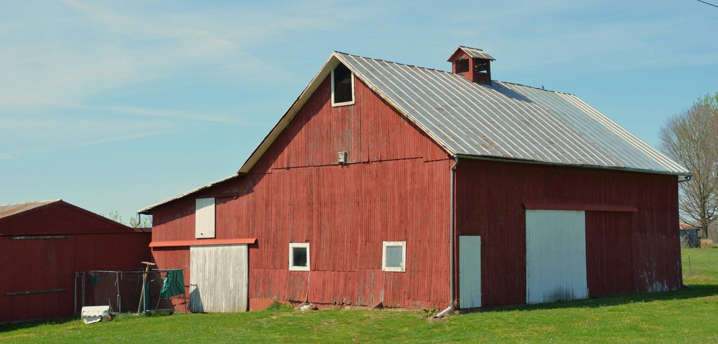 Red barn with a silver ribbed metal roof and a cupola
