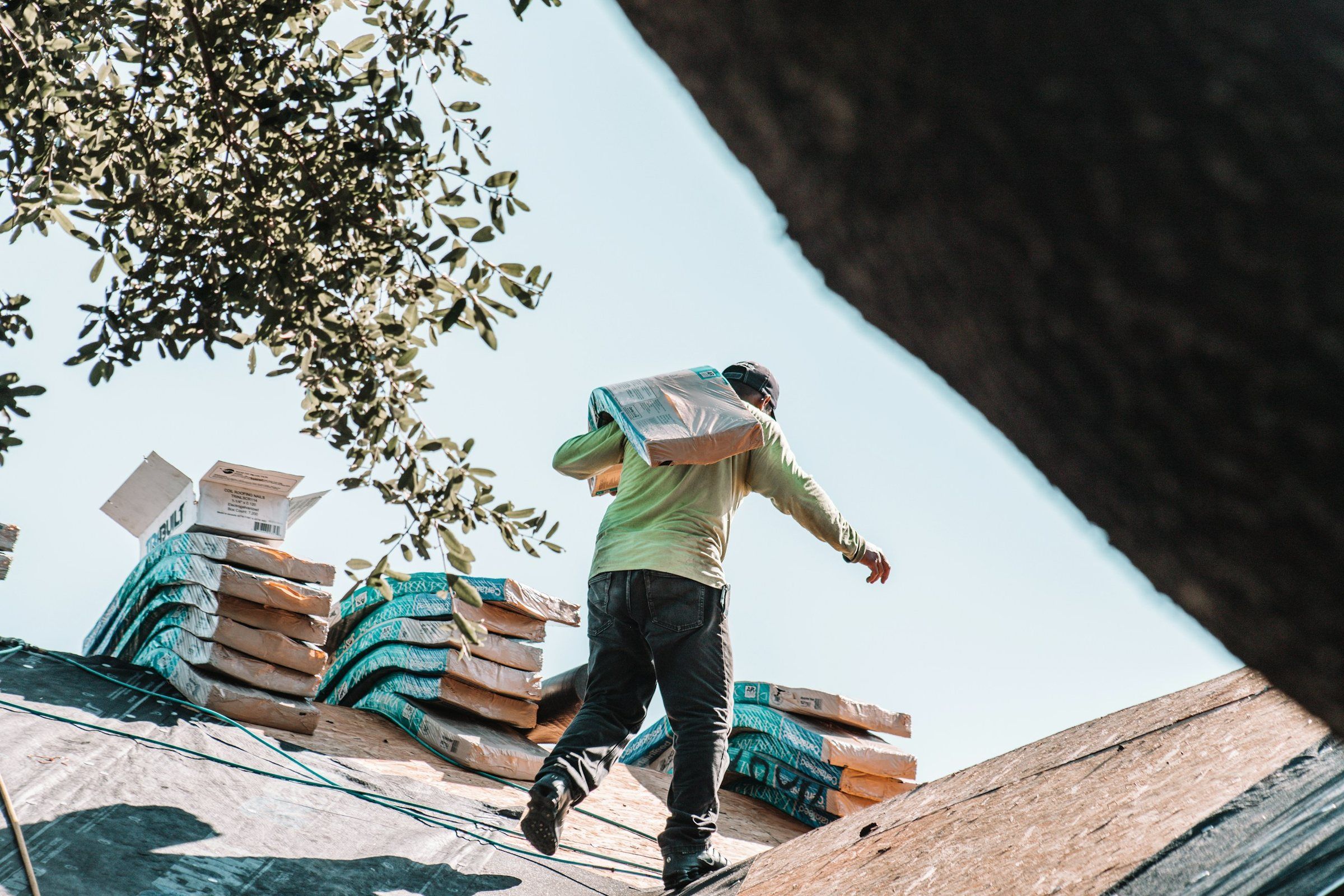 Roofer carrying a bundle of shingles across a stripped roof deck stacked with new bundles