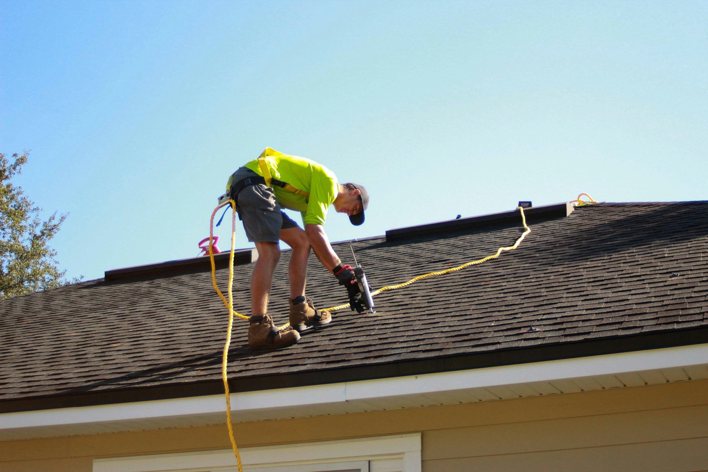 Roofer in a safety harness using a nail gun on an asphalt shingle roof