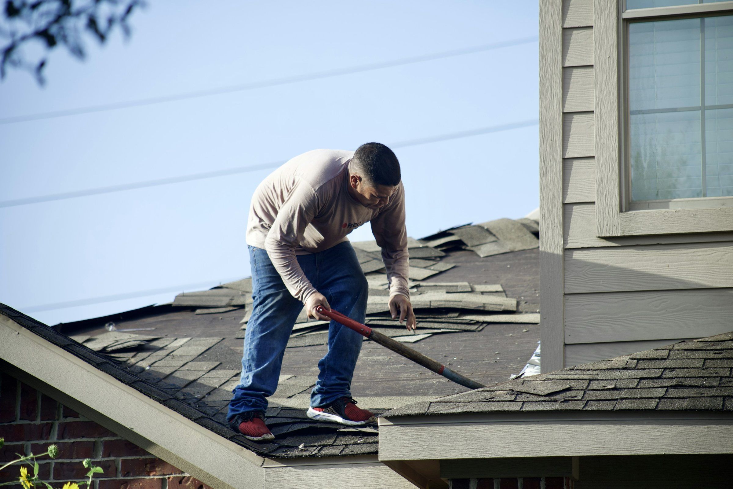 Roofer prying up worn shingles on a residential roof