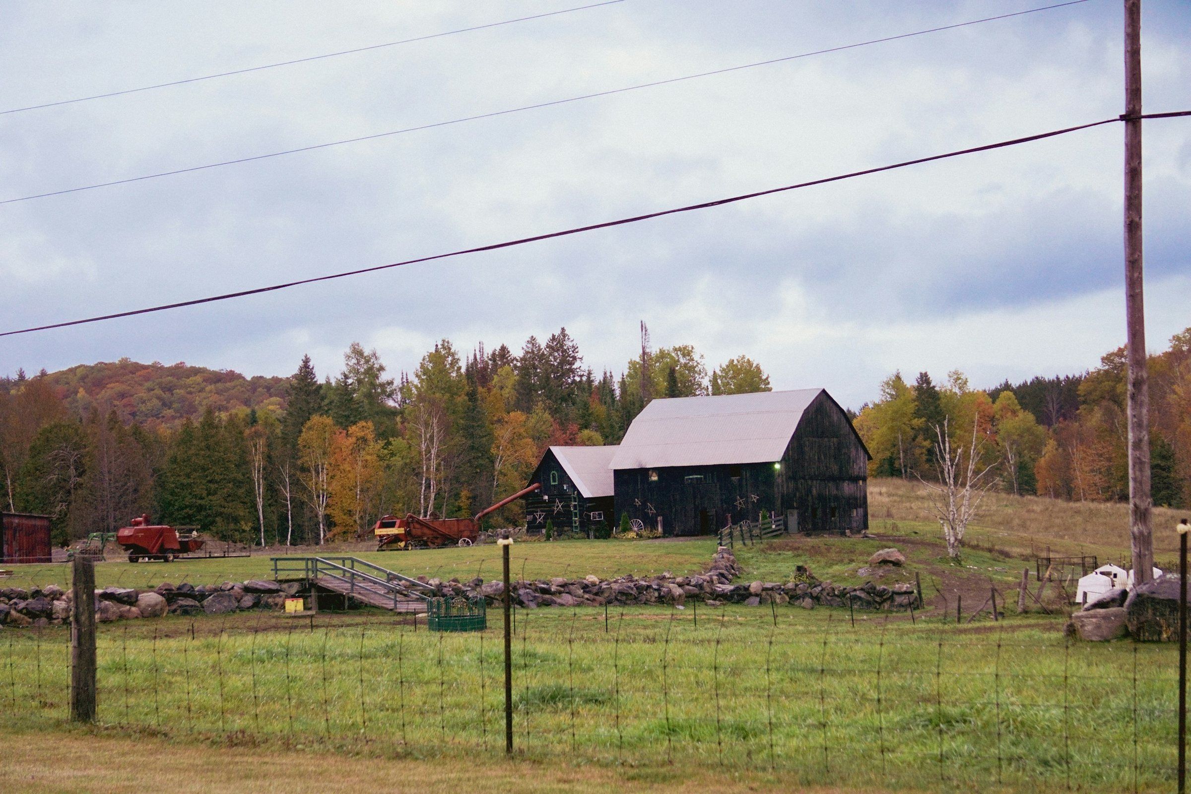 Dark barn with a metal roof beside a fenced pasture and fall trees