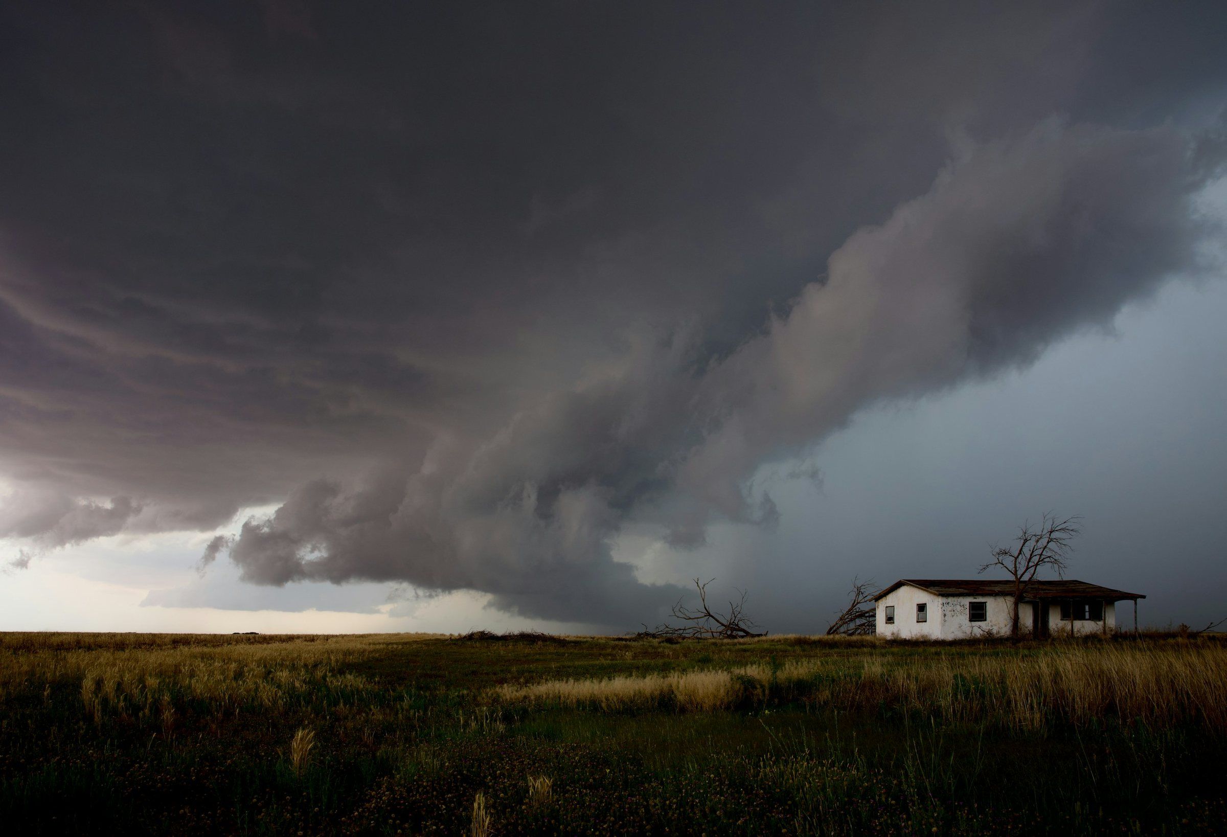 Large storm cloud building over a farmhouse in open country