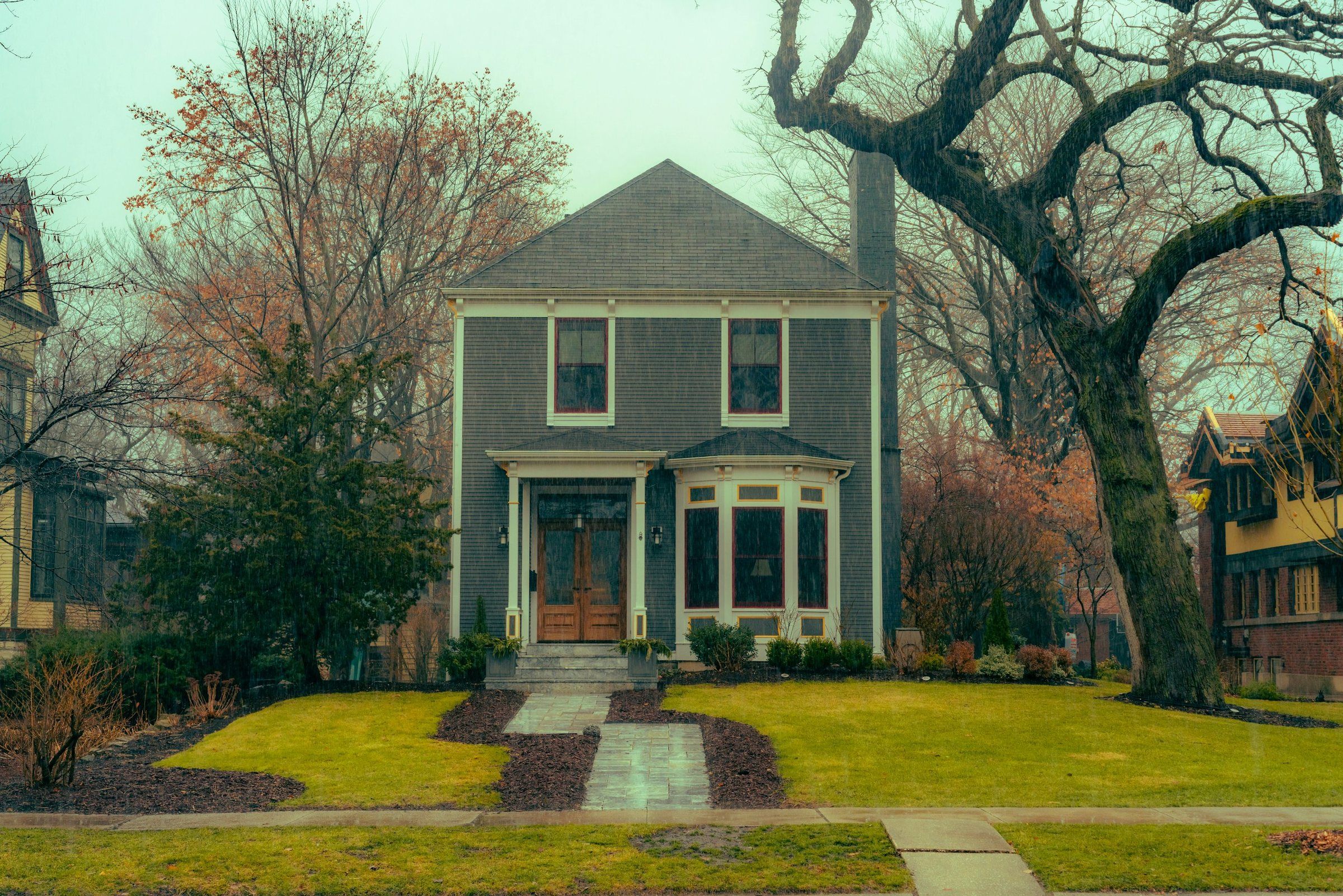 Older two-story home with a hip shingle roof on a damp late-fall day