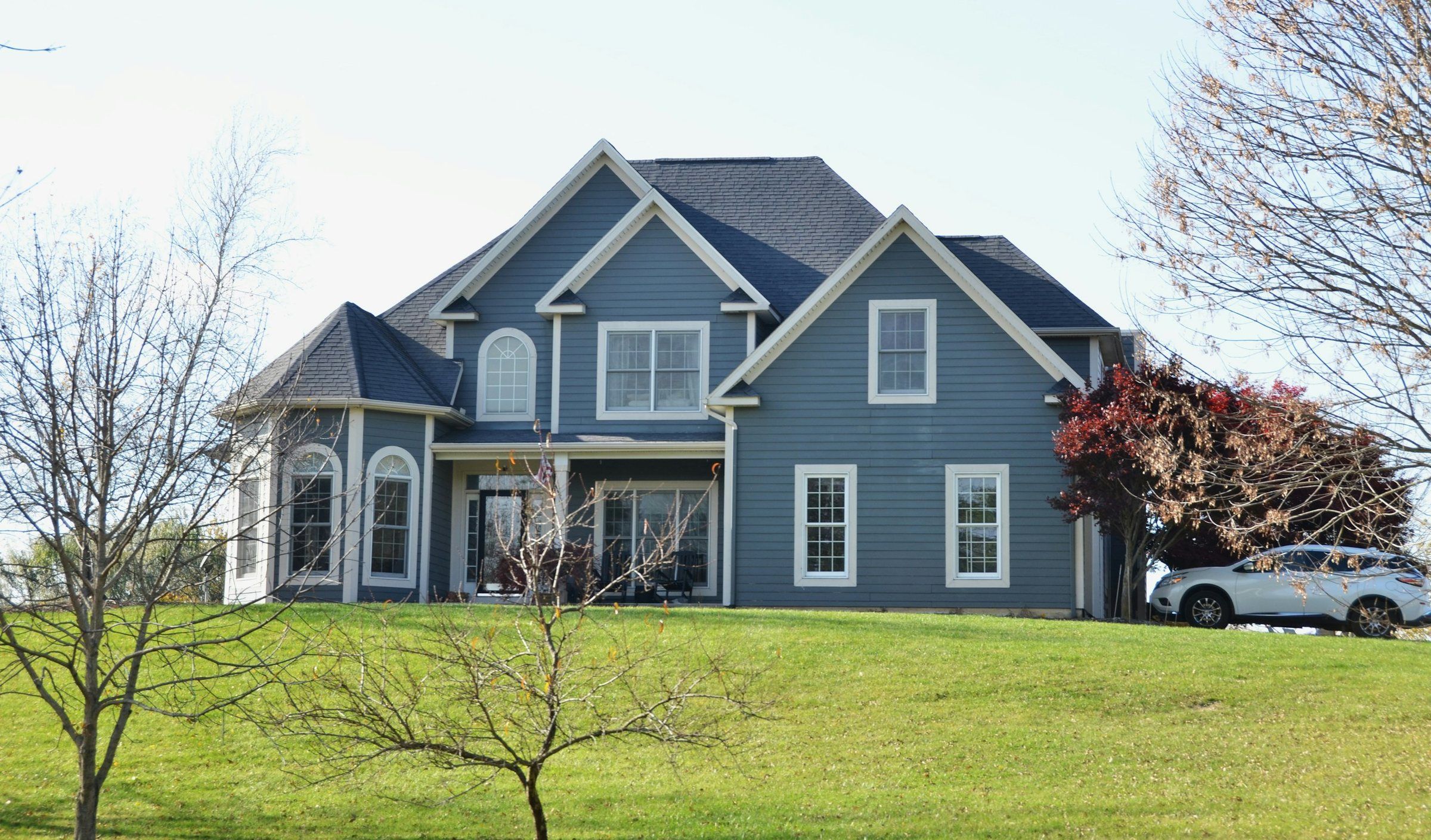 Blue two-story house with a dark gray shingle roof on a grassy lot